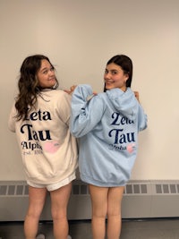 two girls standing next to each other wearing hoodies
