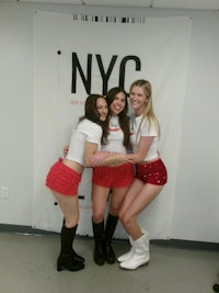 three women posing for a photo in front of a nyc sign